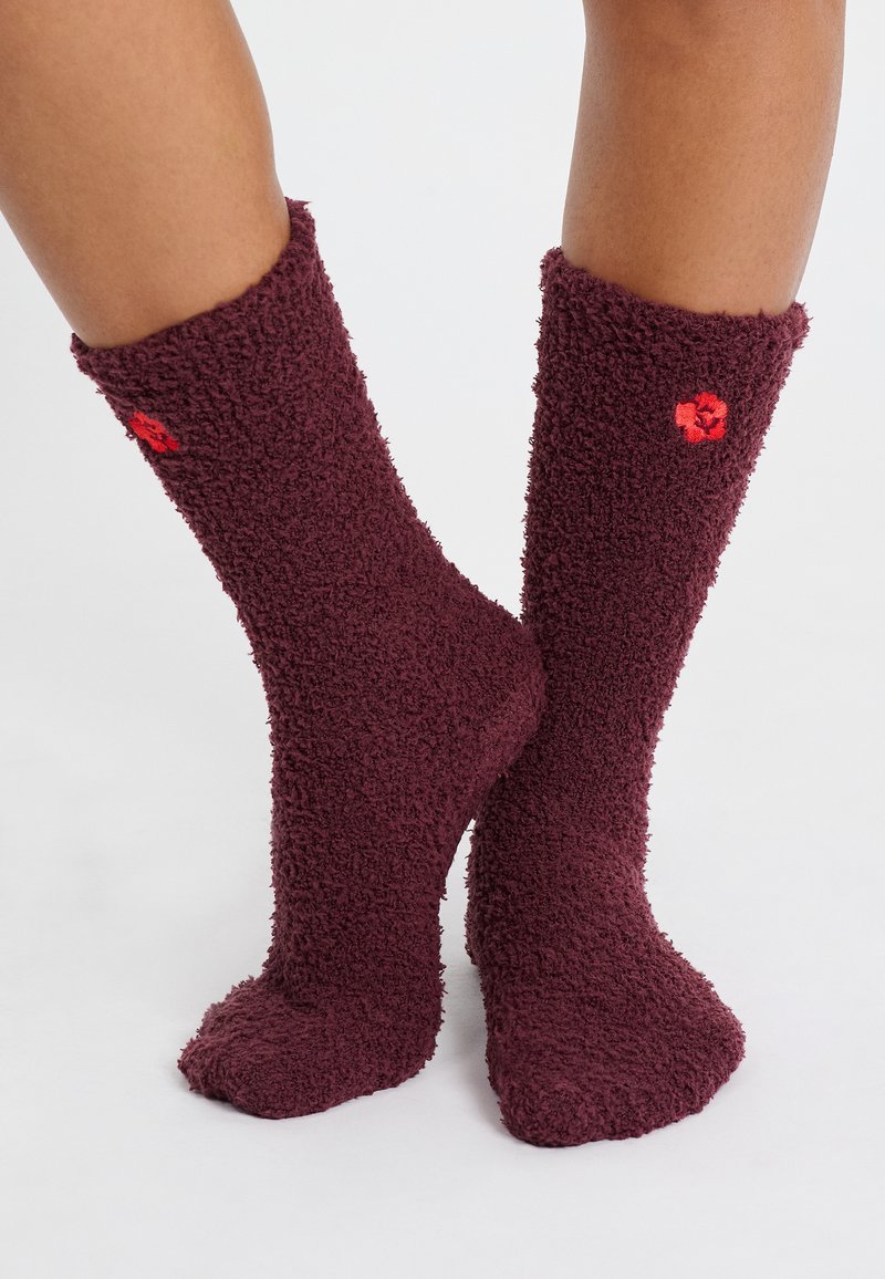 Calze pelose bordeaux realizzate in un materiale texturizzato e morbido; presentano un piccolo accento floreale rosso vicino alla parte superiore.