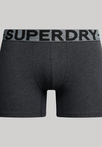 Shorts boxers gris foncé avec une large ceinture élastique portant "SUPERDRY" en lettres noires. Le tissu a une texture lisse.