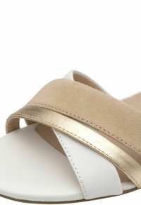 Sandali leggeri con suola in pelle bianca, cinturino in suede beige e un accento metallico dorato. Presentano un design a fasce incrociate per una vestibilità sicura.