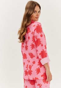 Růžová blůza s květinovým potiskem a červenými květy, tříčtvrteční rukávy, volný střih a ohrnuté manžety, navržena pro ležérní vzhled.