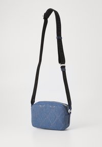 Borsa a tracolla in denim con motivo a diamante, chiusura con zip, tracolla nera regolabile con logo e accenti blu. Forma compatta e rettangolare.