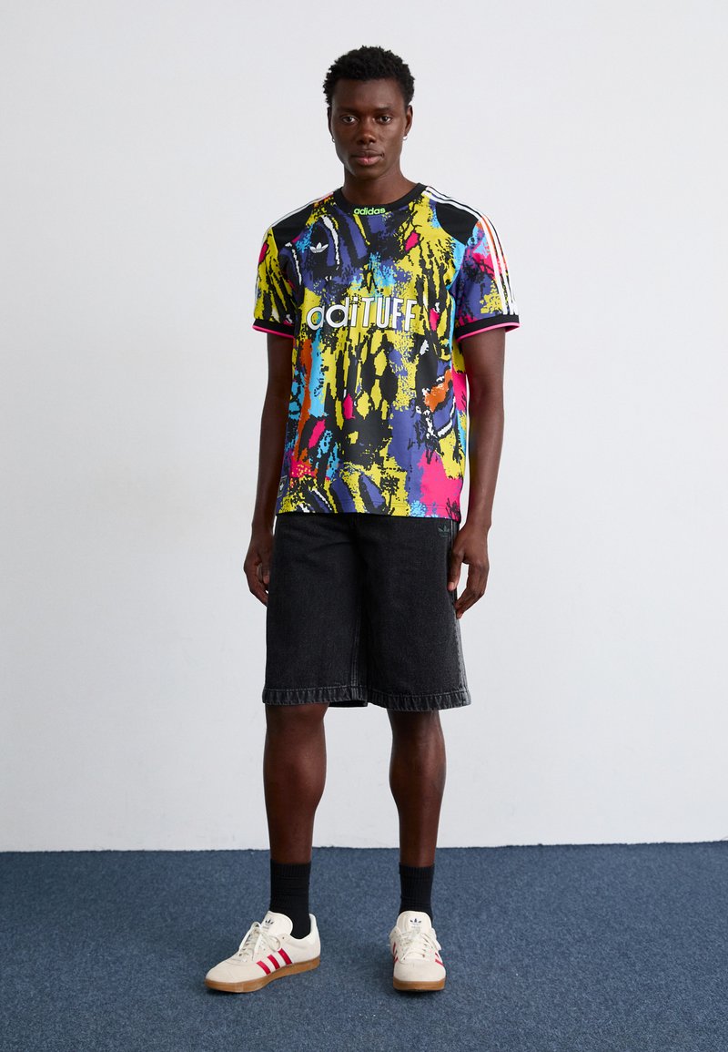 Barevný krátký rukáv dres s černým a neonovým abstraktním vzorem, se zeleným akcentem na límci a bílým textem. Nosit s tmavými šortkami a teniskami.