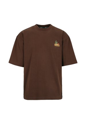 Braunes, übergroßes T-Shirt mit kurzen Ärmeln und kleinem Brustmotiv eines Kaktus in einer geschichteten Wüstenlandschaft.