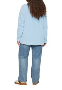 Lichtblauw langarm shirt met verlaagde schouders, gecombineerd met losse lichtblauwe spijkerbroek en casual bruine platform instapschoenen.