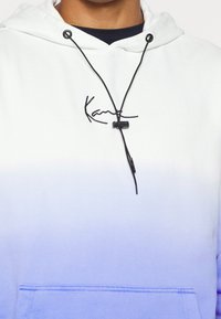 Hooded sweatshirt in a white to purple gradient, featuring black drawstrings and a small embroidered logo at the chest.