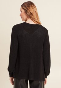 Pull noir à manches longues avec un motif de tricot texturé, coupe décontractée et poignets côtelés. Présente un léger éclat et un dos en V.