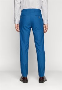 Prispôsobené modré nohavice z hladkej látky, slim fit, s dvoma zadnými vreckami a gombíkovými detailami, skombinované s tmavými koženými topánkami.