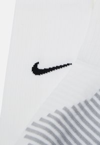 Hvide sportsstrømper med en sort Nike swoosh-logo, der har ribbet tekstur og grå stribede detaljer på den ene side.