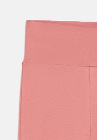 Leggings rosas hechos de tela acanalada, con una cinturilla ancha y una textura suave, con un brillo sutil y sin patrones o acentos visibles.