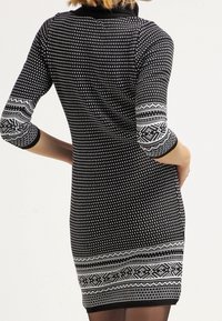 Abito bianco e nero con maniche a tre quarti, caratterizzato da un design a pois e una banda geometrica intrecciata all'orlo.