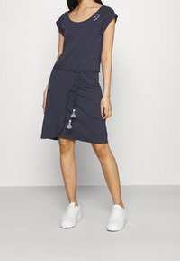 Marinrandig klänning med rundad halsringning, korta ärmar, dragsko i midjan och fransdetaljer. Matchas med vita sneakers.