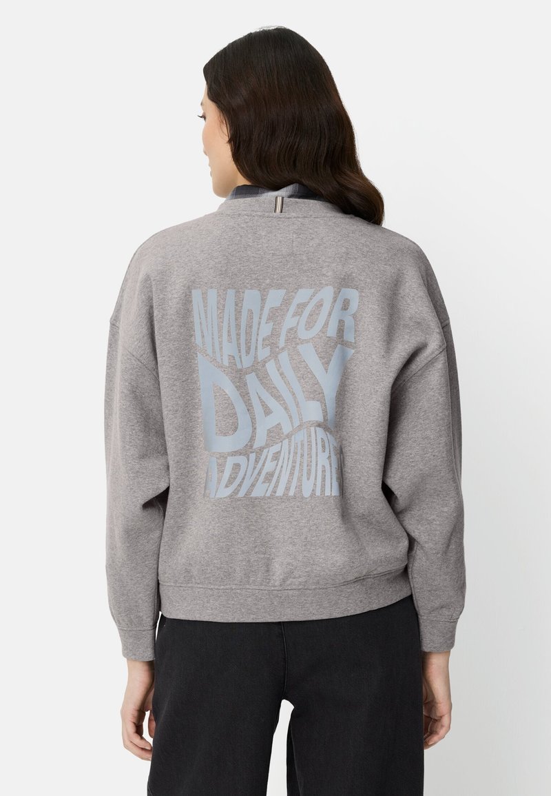 Grijze sweater met gestructureerde stof, een losse pasvorm en de tekst "MADE FOR DAILY ADVENTURE" in lichtblauw op de achterkant.