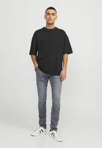 Crna oversized pamučna majica, svijetlosive slim-fit traperice i bijele tenisice s crnim detaljima. Jednostavna, ležerna odjeća.