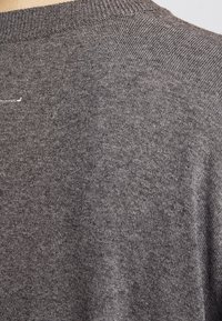 Gray knit sweater with a round neckline. The texture is smooth with a subtle pattern, featuring a small stitched detail at the back.