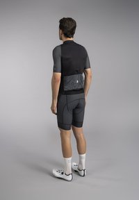 Zwarte fietsshirt met korte mouwen en een lichtgrijze achterzak, gecombineerd met donkergrijze shorts en witte fietsschoenen, met een getailleerd ontwerp.