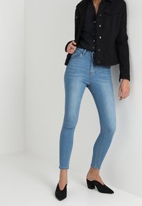 Jeans in denim leggero blu abbinati a un giubbotto di denim nero cropped e tacchi a punta neri. Tessuto liscio con un design aderente.