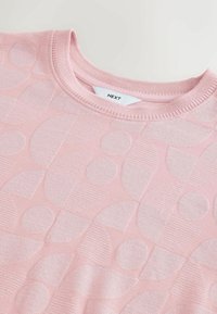 Haut en maille rose doux avec un col rond, présentant un motif géométrique subtil de cercles et de demi-cercles aux textures variées.