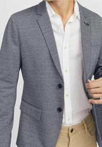 Navy und weiß karierter Blazer, taillierte Passform, Ein-Knopf-Verschluss, zwei Vorderaschen, über einem weißen Hemd getragen, kombiniert mit Khakihosen.