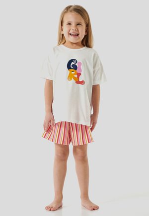 T-shirt en coton blanc avec un graphique coloré "FILLE" ; associé à un short à rayures dans des teintes rouges, roses et jaunes. Enfant debout pieds nus, souriant.