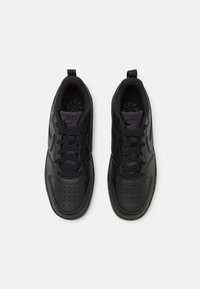 Schwarze Nike-Sneaker mit einem glatten Lederoberteil, Schnürverschluss, durchbrochener Zehenpartie und kontrastierender texturierter Innenauskleidung.