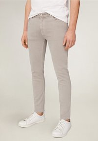Pantalones ceñidos de color gris claro con una suave mezcla de algodón, que cuentan con cinco bolsillos y una cremallera clásica. Combinados con zapatillas blancas.