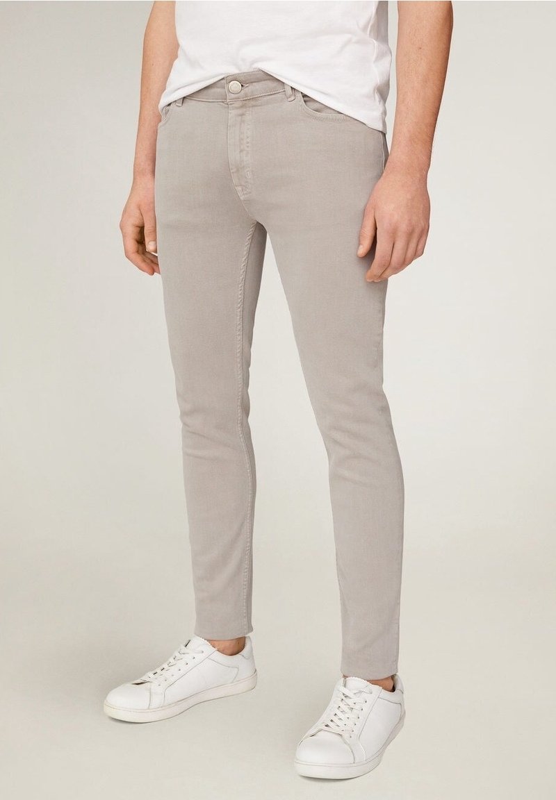 Pantalones ceñidos de color gris claro con una suave mezcla de algodón, que cuentan con cinco bolsillos y una cremallera clásica. Combinados con zapatillas blancas.