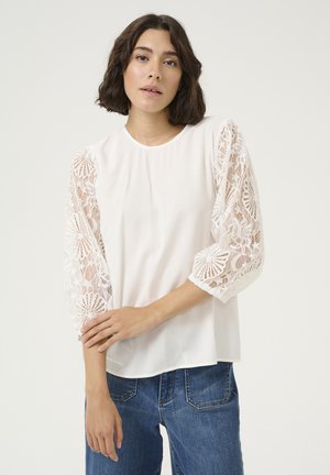 White blouse with lace puff sleeves featuring floral patterns. Soft fabric, round neckline, and loose fit, paired with blue jeans.