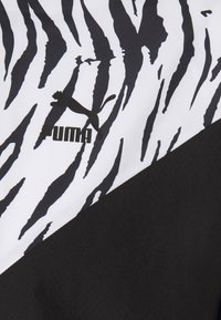 La tela de ropa deportiva Puma presenta un patrón de rayas de cebra en blanco y negro con una sección sólida en negro. Incluye un distintivo logo de Puma en negro.