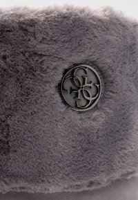 Bande en fourrure synthétique grise avec un accent de logo métallique rond. La texture douce et l'éclat naturel rehaussent les détails et l'apparence du produit.