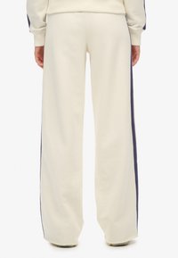 Crèmekleurige joggers met een relaxte pasvorm, voorzien van donkere navy zijstrepen en een zachte textuur, die net boven de schoenen eindigen.