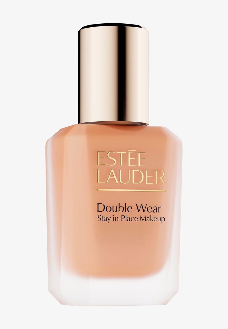 Fond de teint Estee Lauder Double Wear dans une bouteille en verre transparent avec un bouchon doré. Le liquide est d'une teinte beige pêche. Le texte est en doré et noir.