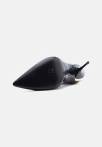 Μαύρη στιλέτο γόβα με μυτερή μύτη, γυαλιστερό φινίρισμα και αντίθετη μπεζ σόλα, που αναδεικνύει λεία υφή και κομψή σιλουέτα.