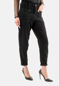 Pantalones de pana negra de talle alto con pu�ños enrollados, bolsillos frontales y detalles de presión plateados, combinados con tacones negros de punta.