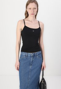Black fitted tank top with thin straps, paired with a light blue denim maxi skirt featuring front pockets and a button closure. Black handbag.