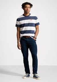 Navy and white striped t-shirt with a logo, paired with dark pants and blue sneakers. The outfit features a relaxed fit and casual design.
