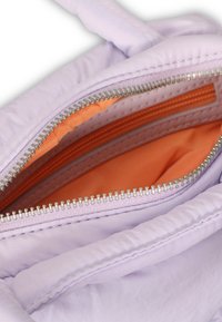 Intérieur d'un sac lilas, avec un revêtement orange. Compartiments zippés avec quincaillerie argentée. Matériau doux et texturé avec des sections rembourrées.