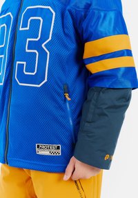 Blaue Netzjacke mit der Nummer "93", gelb gestreiften Ärmeln und schwarzem Reißverschluss. Mit einem Logopatch am Saum und orangefarbenem Reißverschlusszieher.
