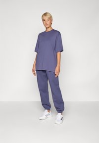 Fialové oversized tričko v kombinaci s odpovídajícími zúženými tepláky. Oblečení má měkkou texturu a volný střih. Spárováno s bílými teniskami.
