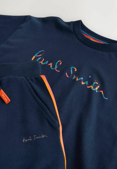 Conjunto de sudadera y pantalones azul marino con el logo colorido de "Paul Smith" y detalle de cremallera naranja en el bolsillo del pantalón.
