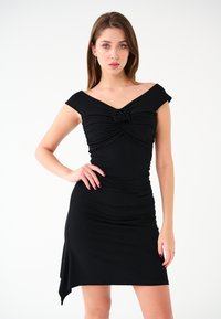 Czarna dopasowana sukienka z krótkimi rękawami, marszczeniem w okolicy biustu i talii, oraz asymetrycznym dołem. Wykonana z elastycznego materiału.