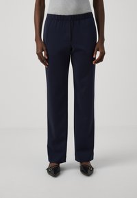 Marineblauwe, rechte broek met een elastische tailleband, gemaakt van een gladde stof. Gecombineerd met puntige zwarte ballerina's.