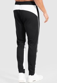 Svarta atletiska joggingsbyxor med vita sidopaneler, elastisk midja och avsmalnande passform. Tillverkade av mjukt tyg med en slät yta.