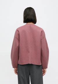 Oversized tröja med långa ärmar i dammigt rosa, tillverkad av mjukt tyg med rund halsringning och minimal sömnad. Har rak skärning och sänkta axlar.