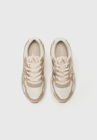 Zapatillas deportivas en color beige y crema con parte superior de malla, acentos texturizados y un cuello acolchado. Cuentan con cordones y una suela de goma.
