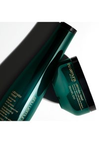 Groene plastic shampoofles en bijpassende haarmasker, beide met zwarte doppen. Labels bevatten gouden tekst die het type product en het gebruik beschrijft.