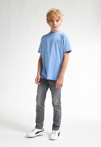 Tricou bleu deschis din bumbac, cu o mică siglă, asortat cu blugi gri și adidași albi cu accente negre.