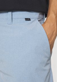 Himmelblaue karierte Shorts mit flachem Bund, Gürtelschlaufen, einer Seiten Tasche und einem kleinen schwarzen Markenetikett in der Nähe des Taillenbands.