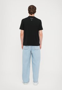 Juoda trumpomis rankovėmis marškinėliai su tiesia kirpte, vilkimi su šviesiai mėlynais plačiomis kojomis džinsais ir baltomis sportbačiais, matoma iš nugaros.