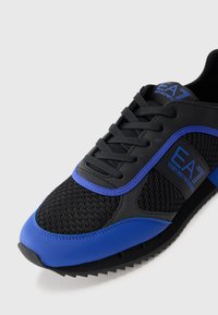 Black and blue sneakers with mesh uppers, rounded toe, rubber sole, and logo accent. Features flat laces and textured panels.