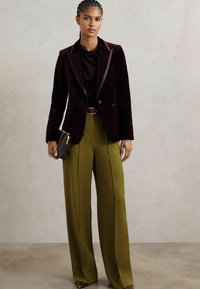 Bordo samet blazer s satenskim reverima, uparen s maslinasto zelenim hlačama širokih nogavica. Uz to ide mala torbica s teksturom.